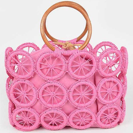 Bright pink woven circle-grid raffia tote with wooden ring handles and removable drawstring pouch.