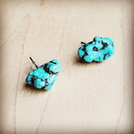 Pair of raw blue turquoise nugget stud earrings with dark veining, displayed on a light wood surface.
