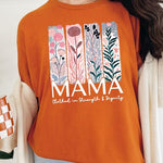 Orange T-shirt with pastel pink and teal floral panel design and bold ‘MAMA’ graphic reading ‘Clothed in Strength & Dignity.