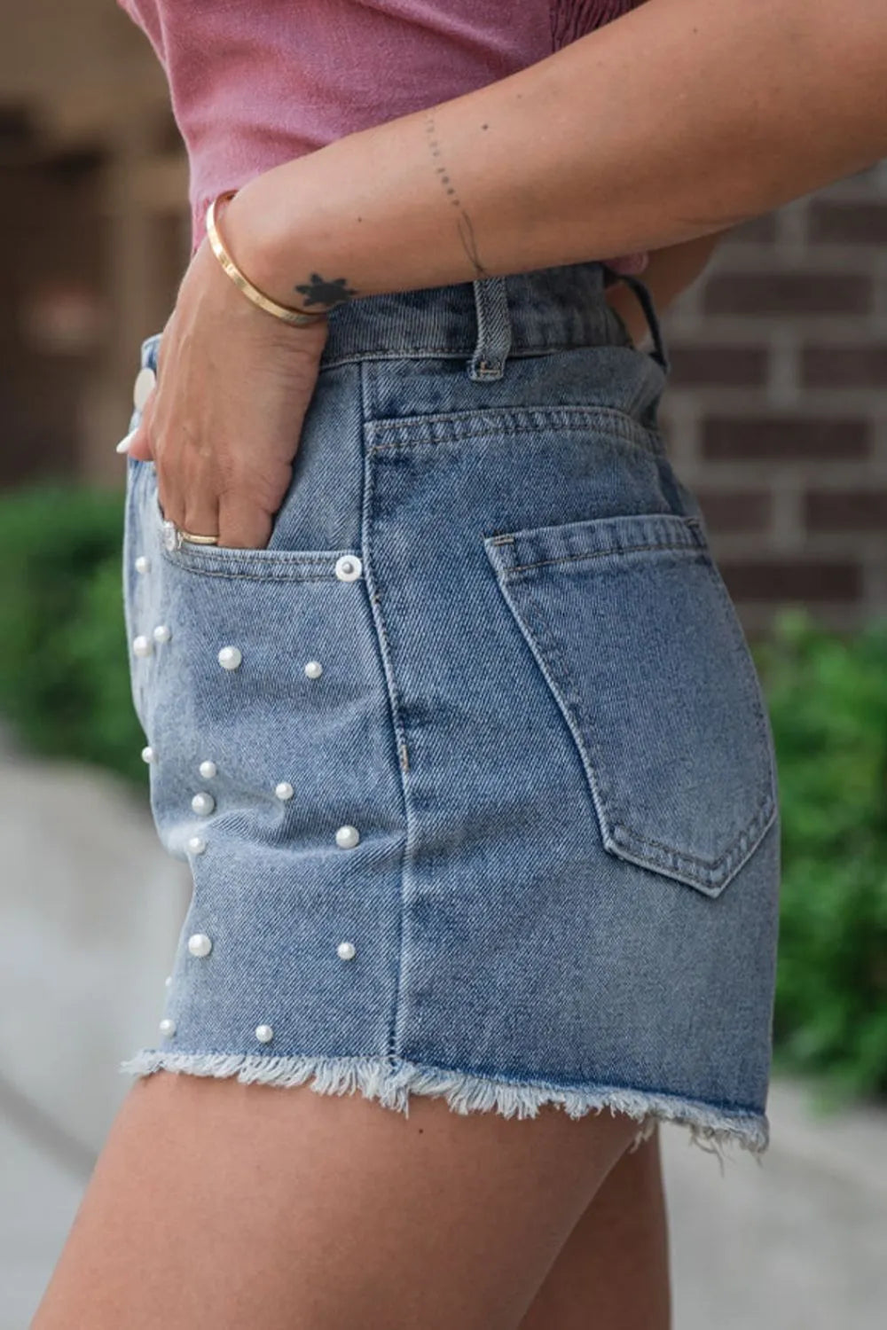 Women's high-waisted denim shorts with faux pearl embellishments and frayed hem – trendy summer jean shorts for casual and chic outfits.