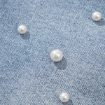 Women's high-waisted denim shorts with faux pearl embellishments and frayed hem – trendy summer jean shorts for casual and chic outfits. Showing the detail.