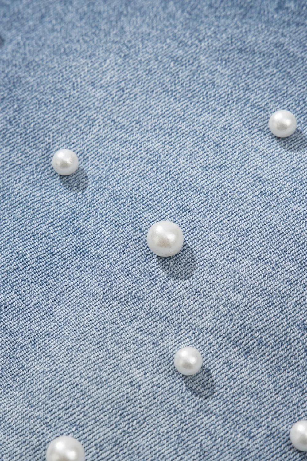 Women's high-waisted denim shorts with faux pearl embellishments and frayed hem – trendy summer jean shorts for casual and chic outfits. Showing the detail.