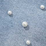 Women's high-waisted denim shorts with faux pearl embellishments and frayed hem – trendy summer jean shorts for casual and chic outfits. Showing the detail.