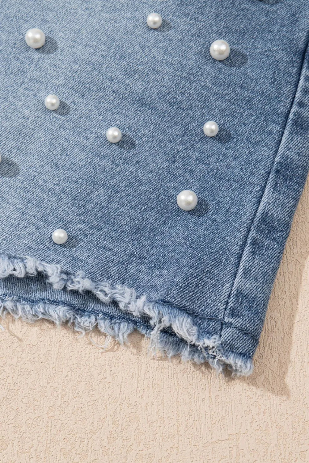 Women's high-waisted denim shorts with faux pearl embellishments and frayed hem – trendy summer jean shorts for casual and chic outfits. Showing the detail.
