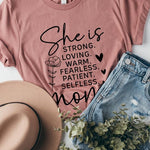 Dusty-rose graphic T-shirt reading ‘She is strong, loving, warm, fearless, patient, selfless—mom’ styled flat-lay with tan fedora, denim shorts, and greenery.