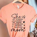 Creamsicle Orange graphic T-shirt reading ‘She is strong, loving, warm, fearless, patient, selfless—mom’ styled flat-lay with tan fedora, denim shorts, and greenery.