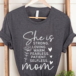Dark Grey graphic T-shirt reading ‘She is strong, loving, warm, fearless, patient, selfless—mom’ styled flat-lay with tan fedora, denim shorts, and greenery.