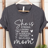 Dark Grey graphic T-shirt reading ‘She is strong, loving, warm, fearless, patient, selfless—mom’ styled flat-lay with tan fedora, denim shorts, and greenery.