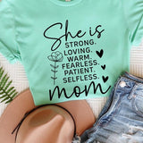 Light Green graphic T-shirt reading ‘She is strong, loving, warm, fearless, patient, selfless—mom’ styled flat-lay with tan fedora, denim shorts, and greenery.