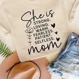 Off White graphic T-shirt reading ‘She is strong, loving, warm, fearless, patient, selfless—mom’ styled flat-lay with tan fedora, denim shorts, and greenery.