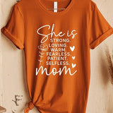 Rusted Orange graphic T-shirt reading ‘She is strong, loving, warm, fearless, patient, selfless—mom’ styled flat-lay with tan fedora, denim shorts, and greenery.