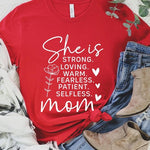 Red graphic T-shirt reading ‘She is strong, loving, warm, fearless, patient, selfless—mom’ styled flat-lay with tan fedora, denim shorts, and greenery.
