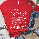 Red graphic T-shirt reading ‘She is strong, loving, warm, fearless, patient, selfless—mom’ styled flat-lay with tan fedora, denim shorts, and greenery.