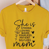 Yellow graphic T-shirt reading ‘She is strong, loving, warm, fearless, patient, selfless—mom’ styled flat-lay with tan fedora, denim shorts, and greenery.