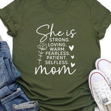 Army green graphic T-shirt reading ‘She is strong, loving, warm, fearless, patient, selfless—mom’ styled flat-lay with tan fedora, denim shorts, and greenery.