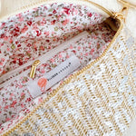 Close-up of floral interior lining with zip pocket inside a glittery woven crossbody bag featuring the Ellison + Young label.