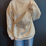 Woman wearing a cream sweatshirt and jeans styled with a sparkly leopard-print woven crossbody belt bag.